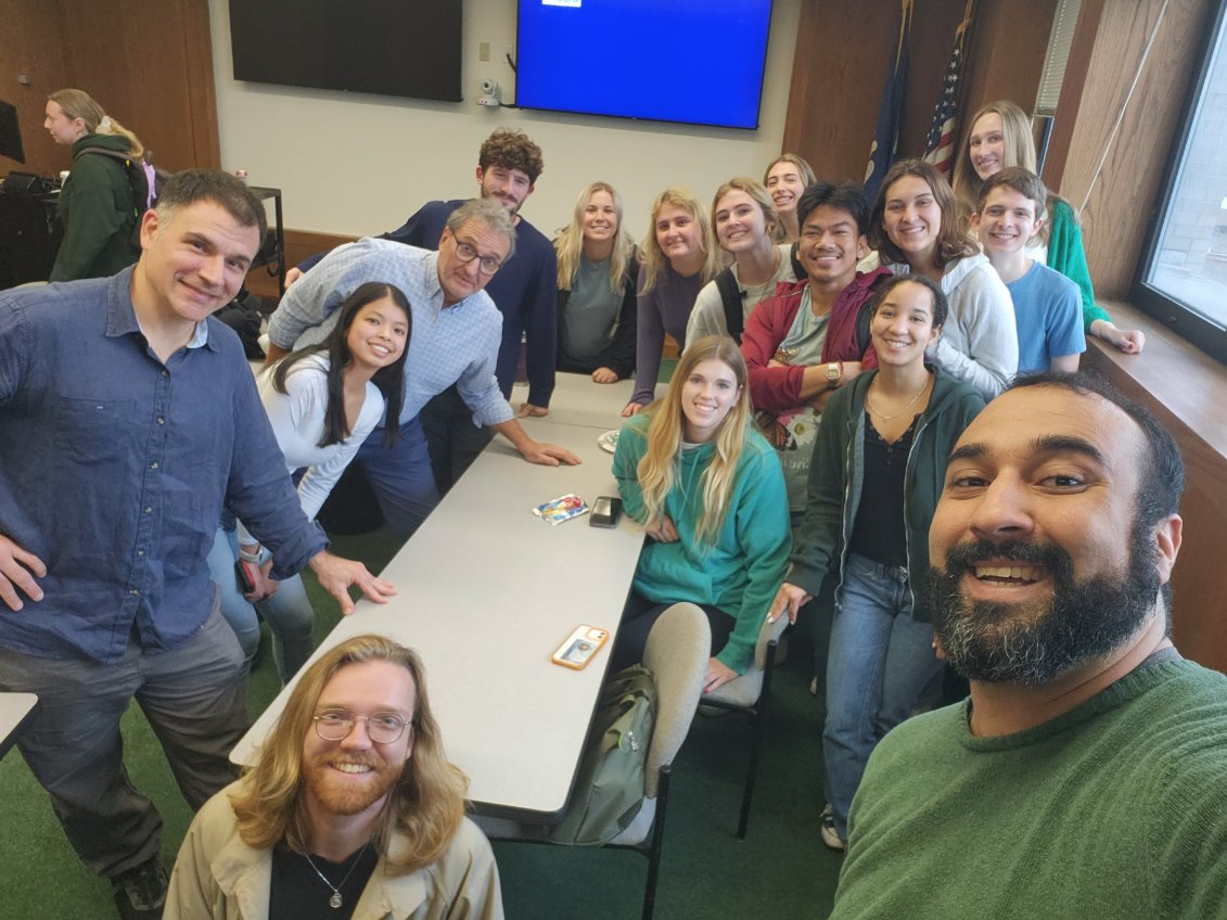 Photograph of a diverse group of people smiling together in a brightly lit room.