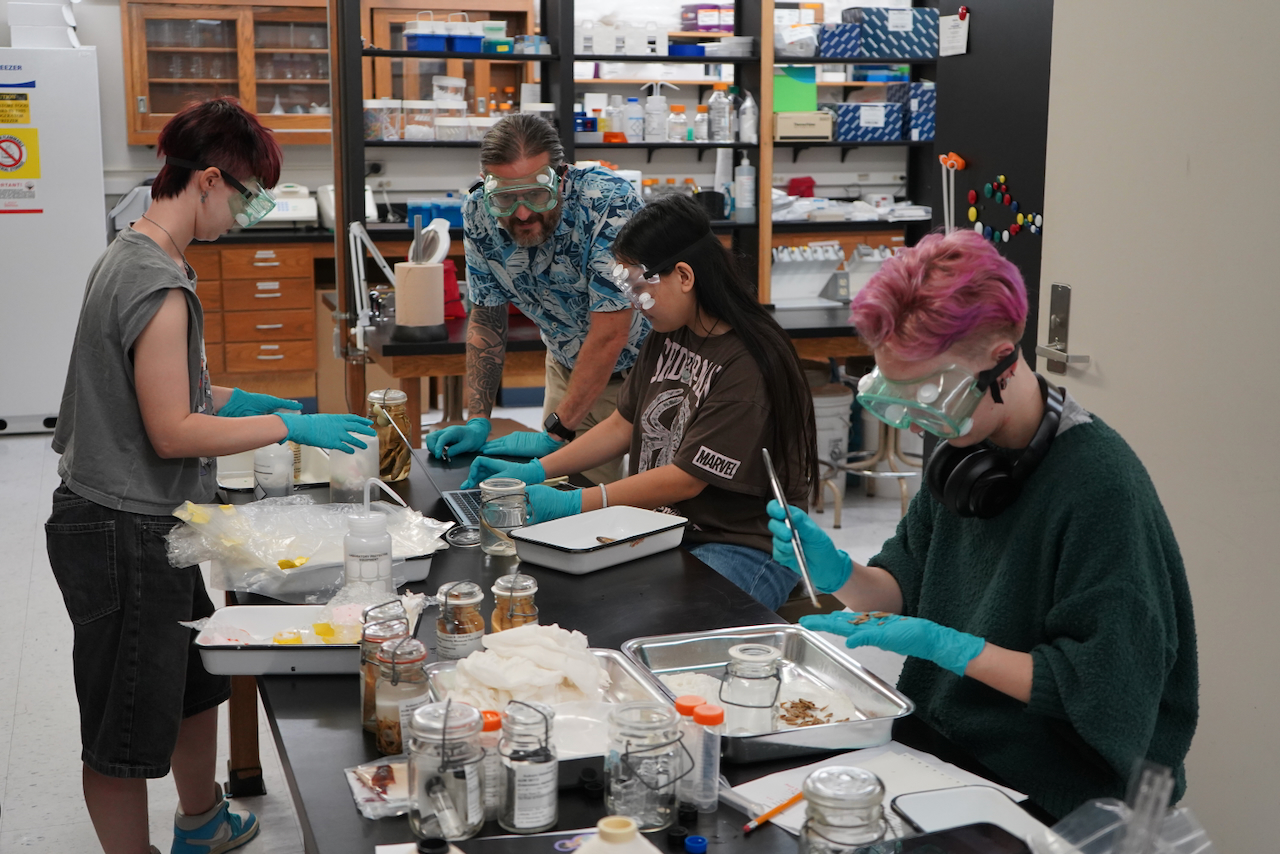 Photograph of students and an instructor working at tables in a brightly lit science lab.