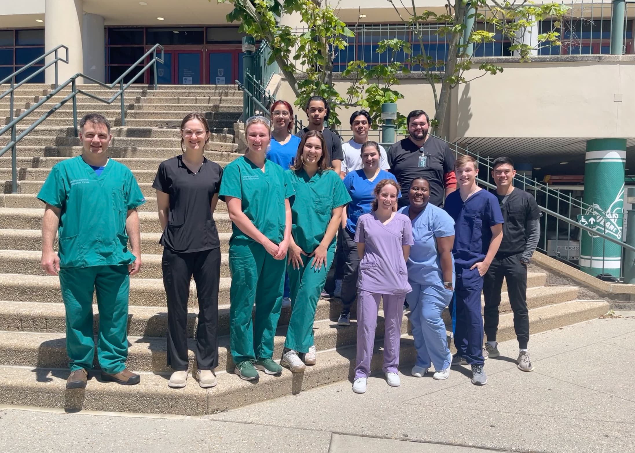 Group of healthcare workers in scrubs pose on outdoor steps in a photograph.