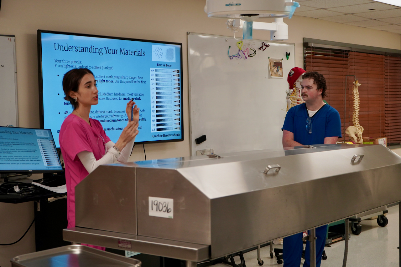 Photograph of a nursing instructor holding a syringe next to a hospital bed.