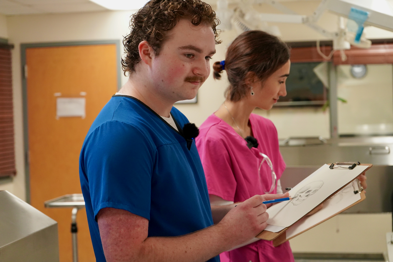 Photograph of two medical workers in scrubs reviewing a clipboard in a hospital.