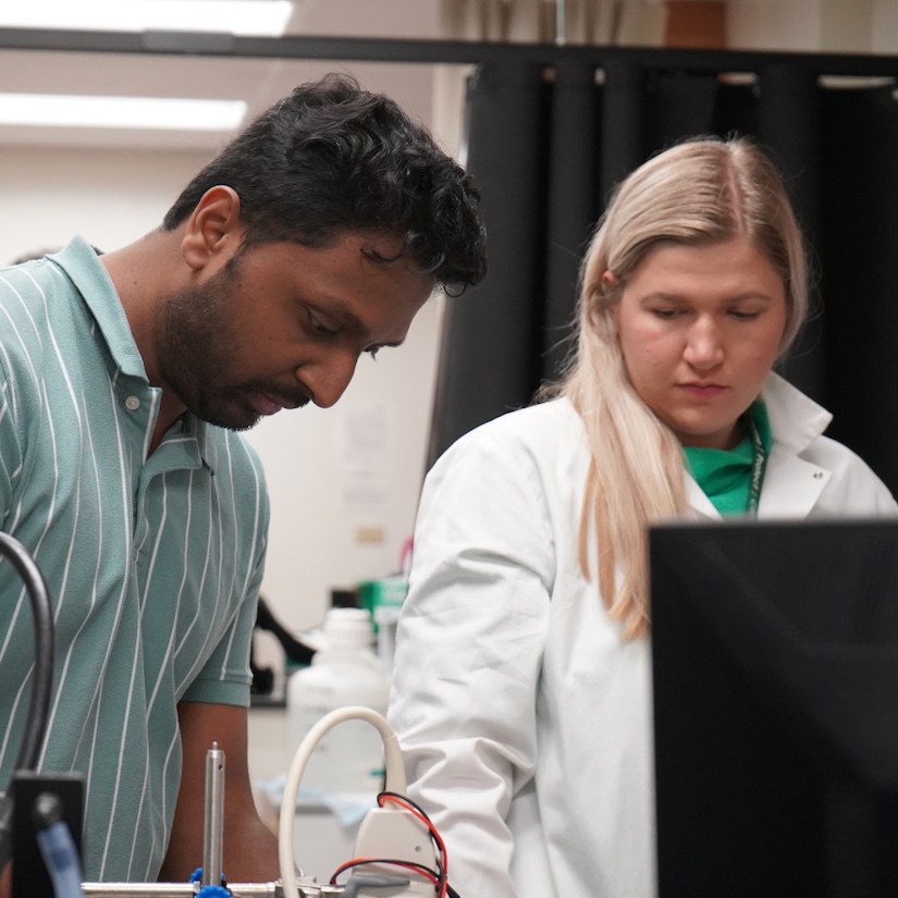 A photograph of two researchers working in a laboratory, focused on equipment.