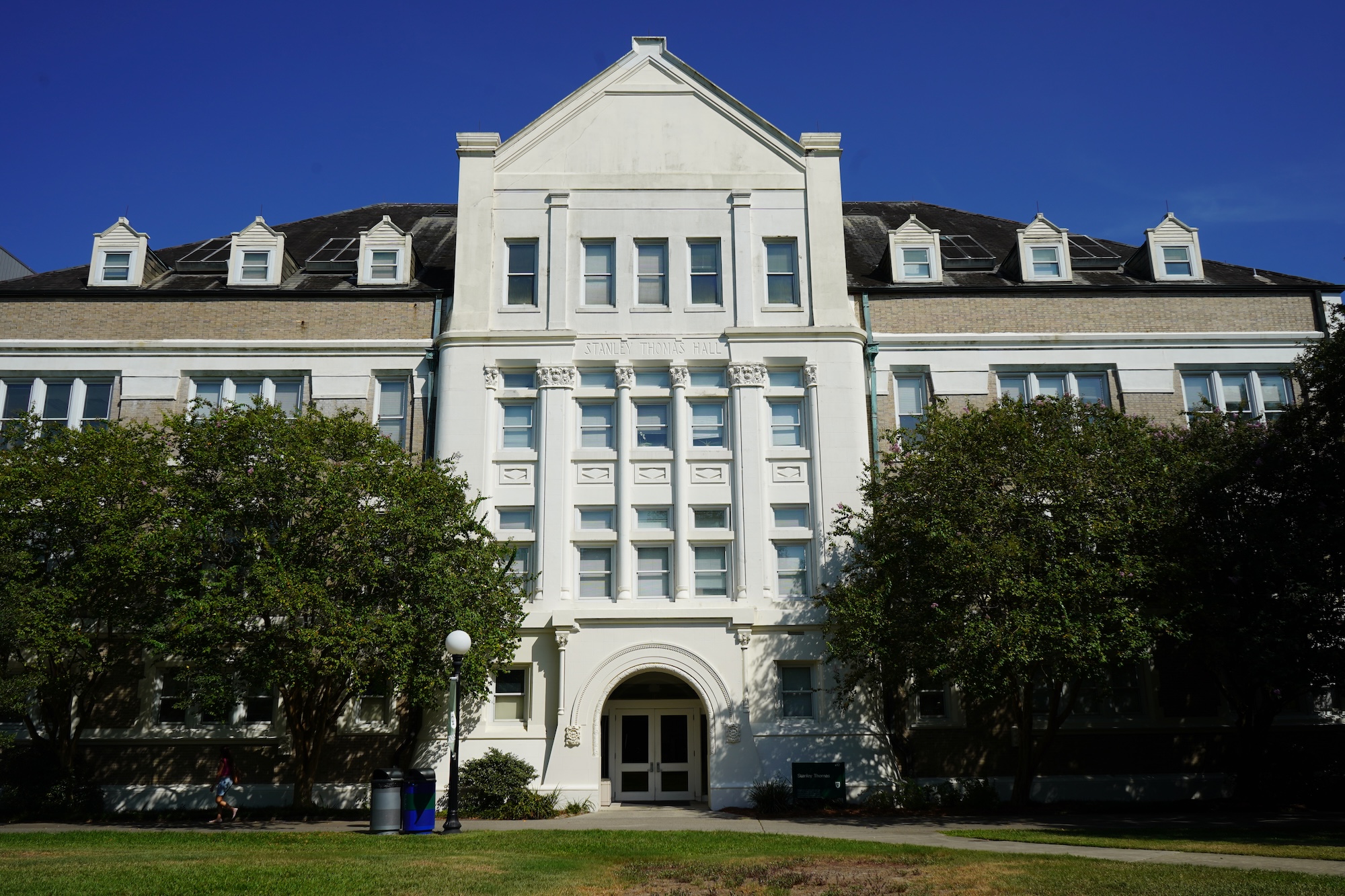 Photograph of a large white and beige historic building under a blue sky, framed by trees.