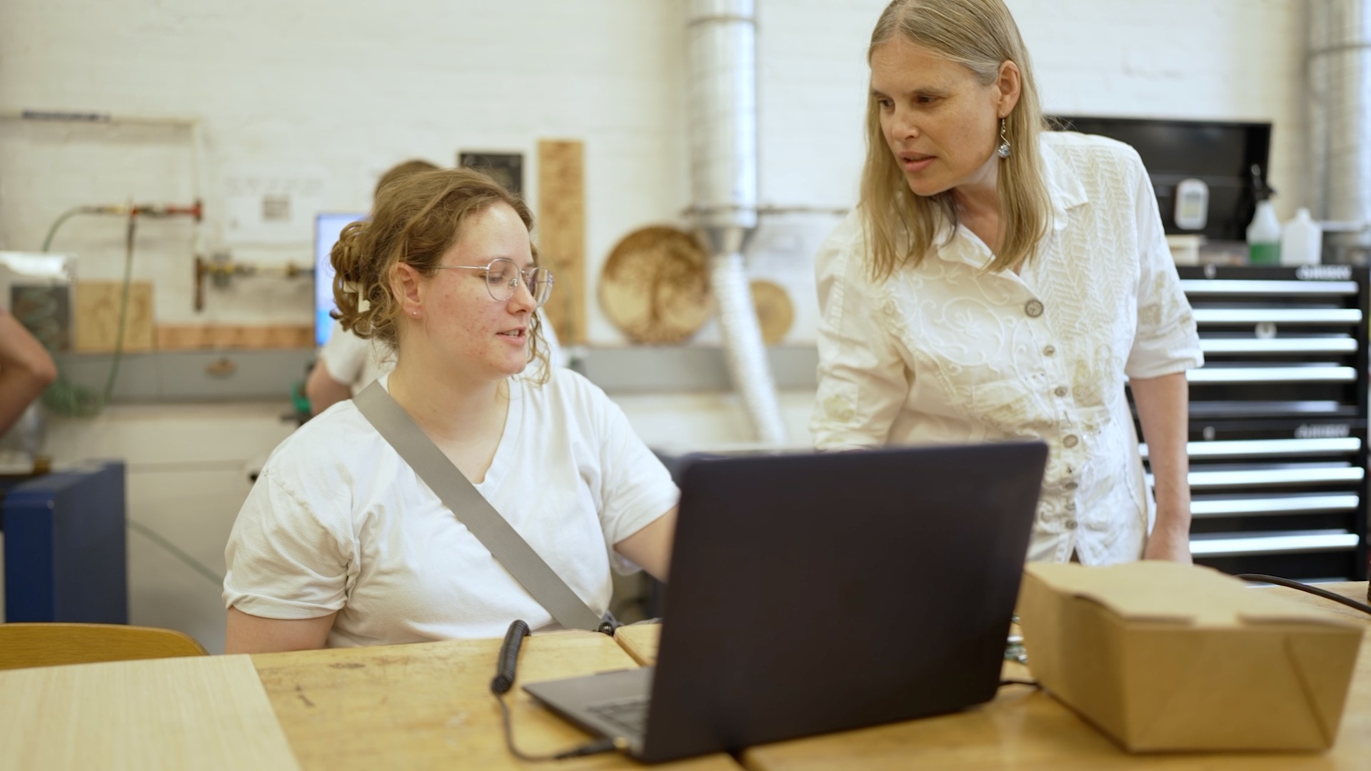 Photograph of two women collaborating in a workshop, looking at a laptop.