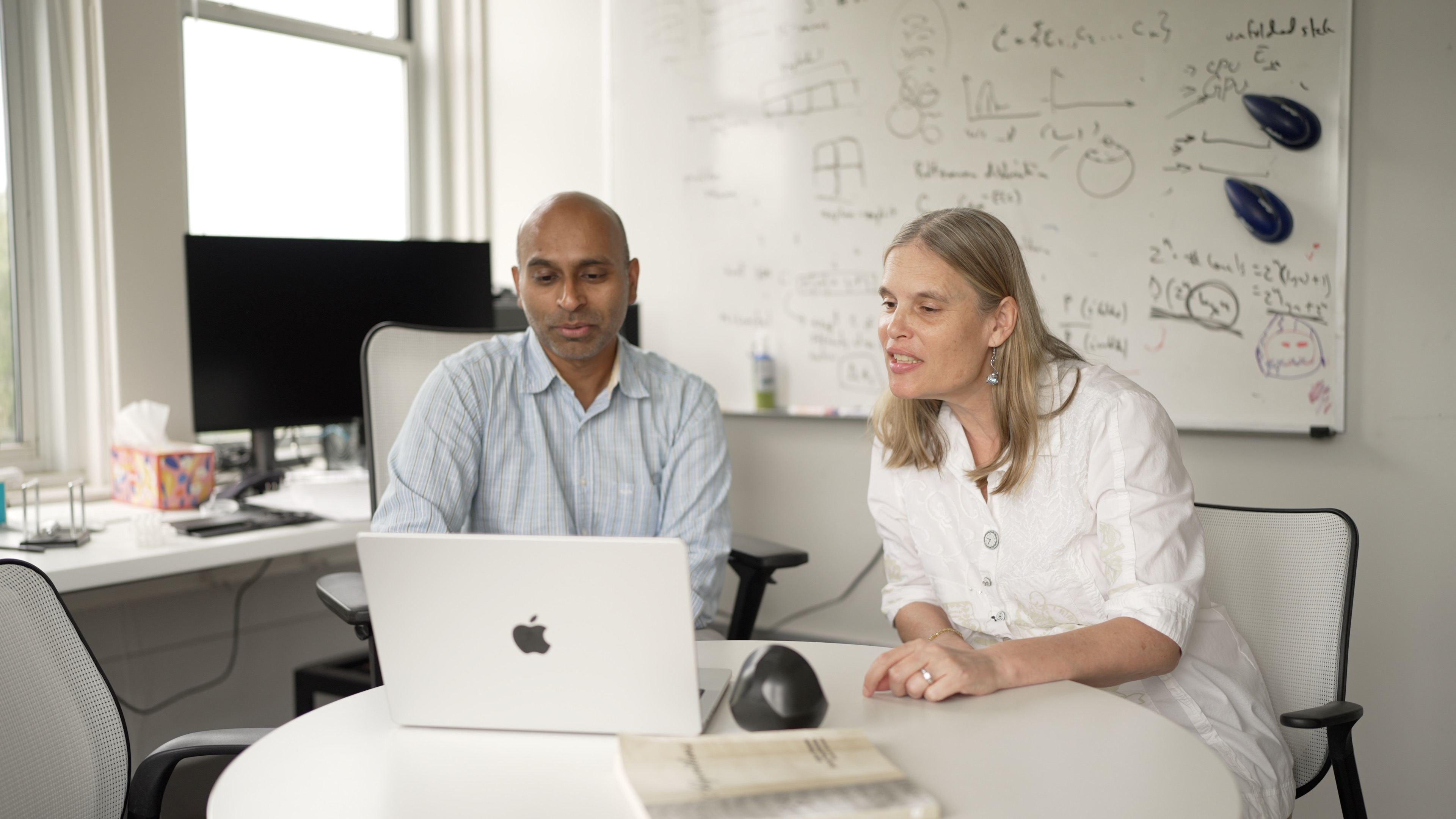 Photo of two people collaborating at a laptop in an office.