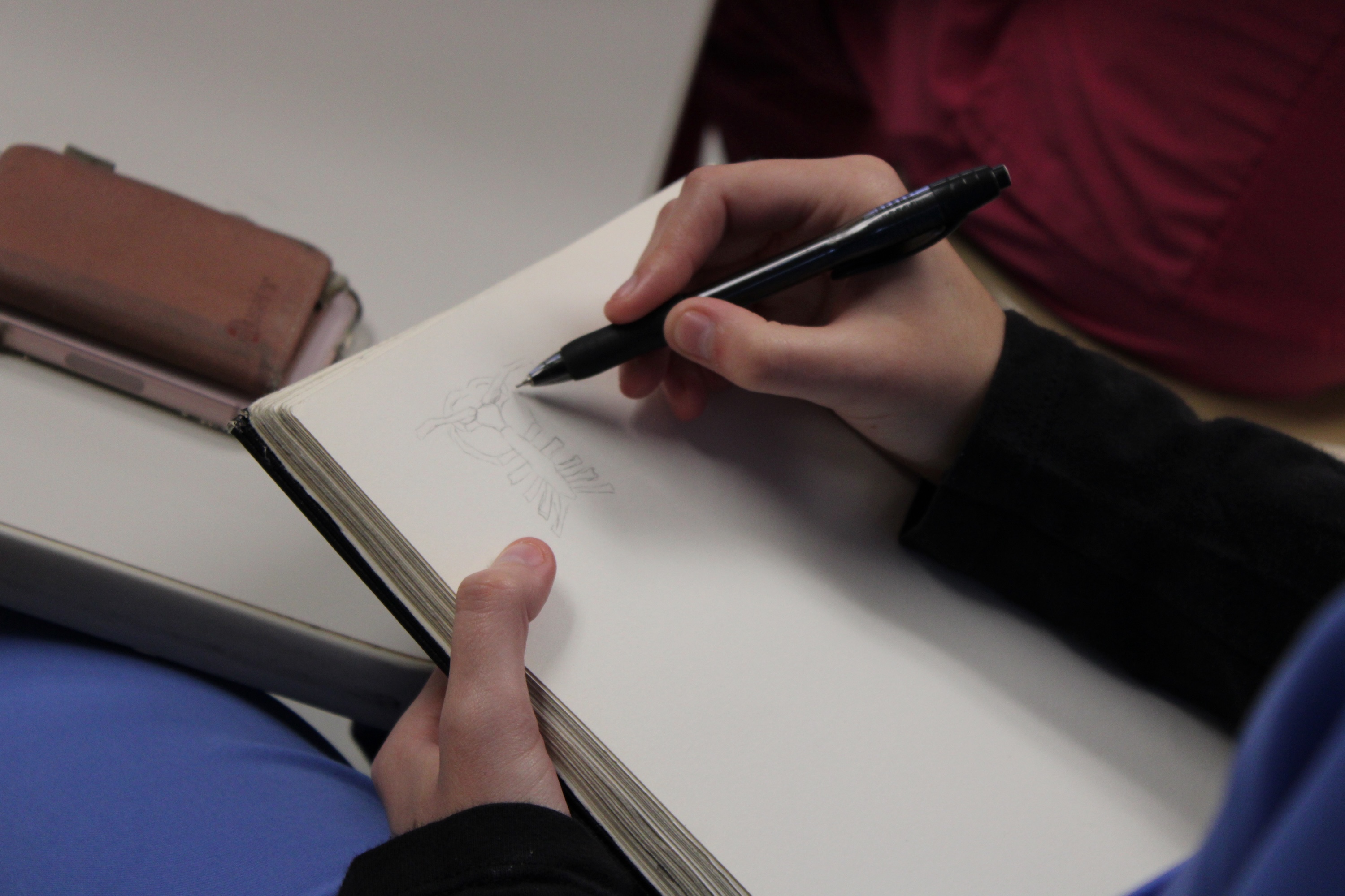 Photograph of a person sketching with a pen in a notebook.