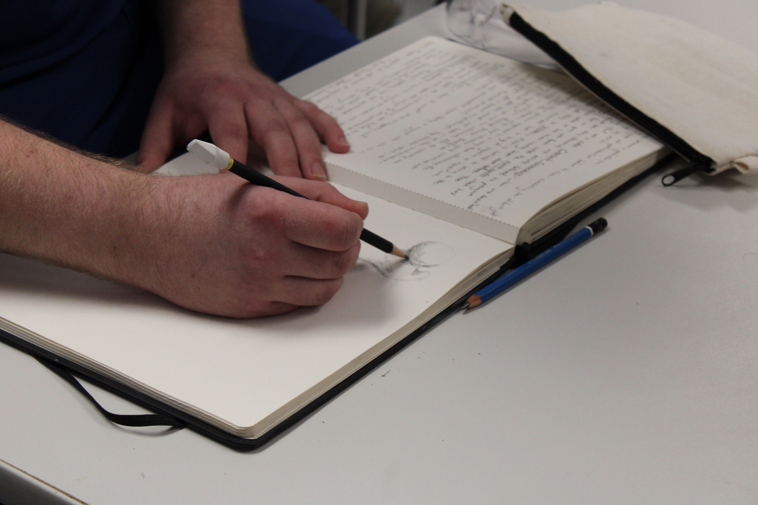 Photograph of a person sketching in a notebook with a pencil.