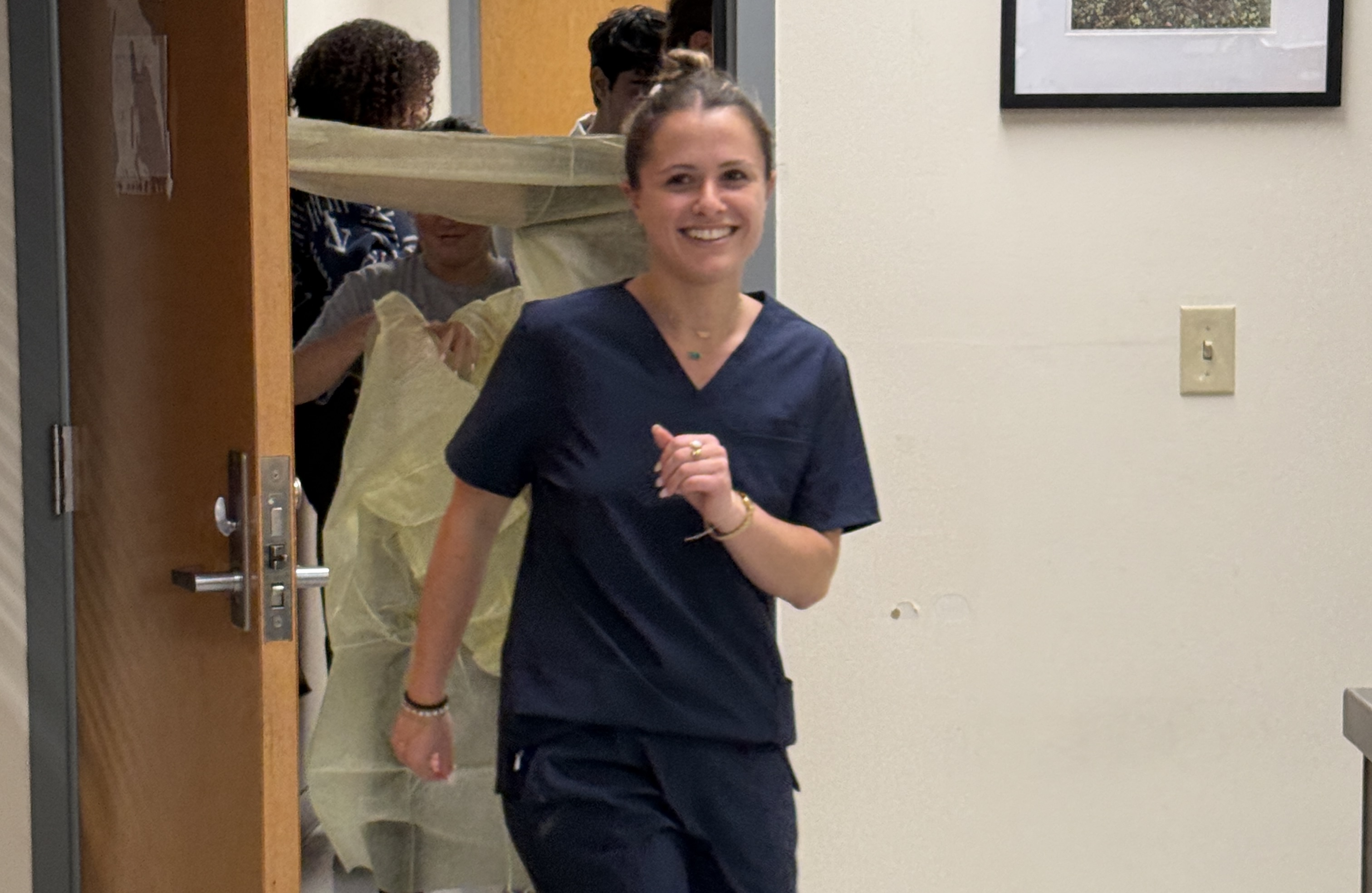 Photograph of a smiling nurse in navy scrubs running down a hallway.