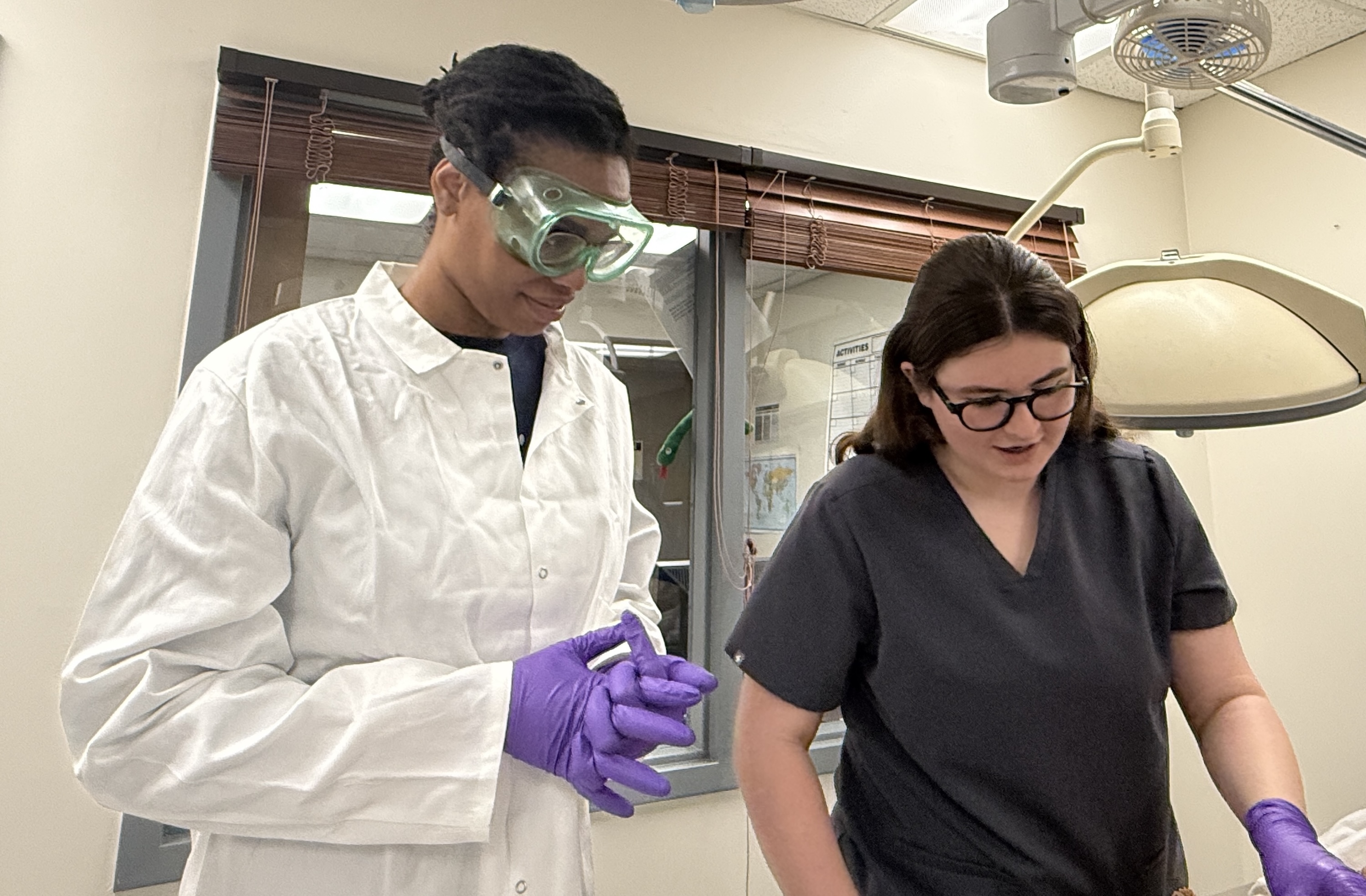 Photograph of two students wearing protective gear in a lab.