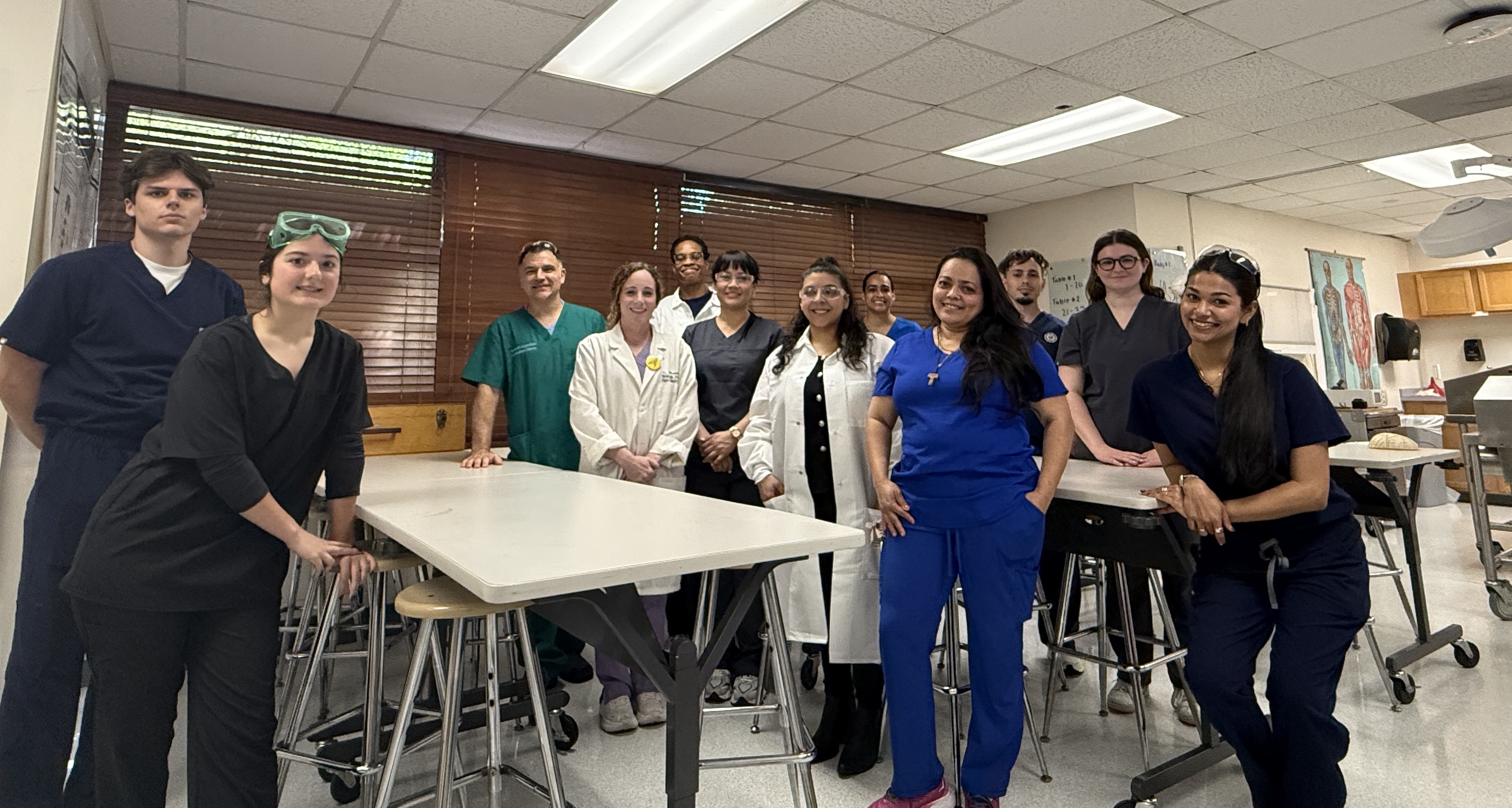 A group of medical students in scrubs pose together in a classroom.