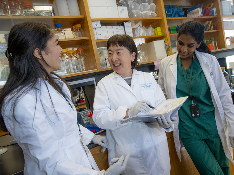 Photograph of three diverse scientists in a lab, discussing and reviewing notes.