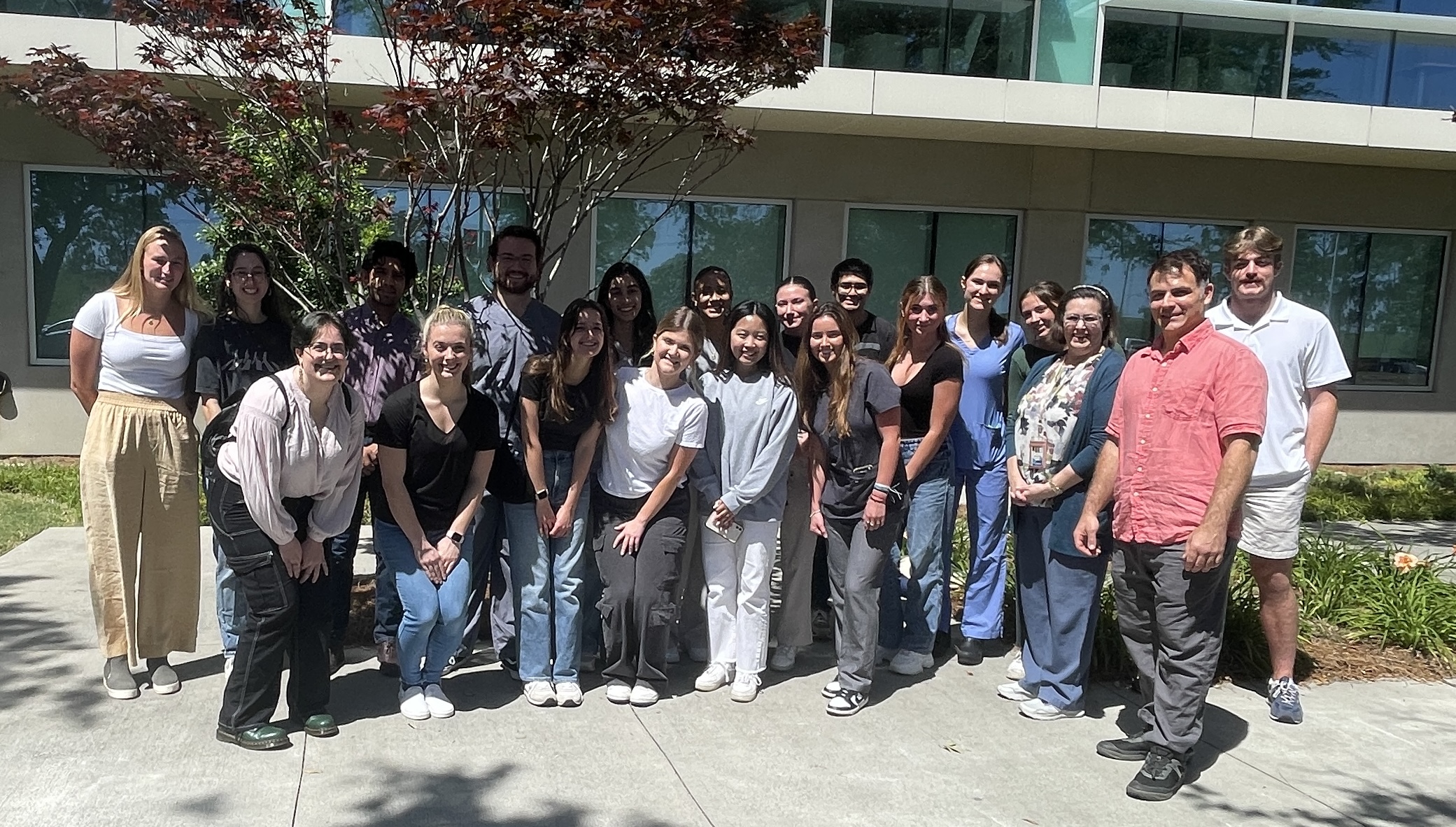 A group of young adults and adults posing outside a building on a sunny day.