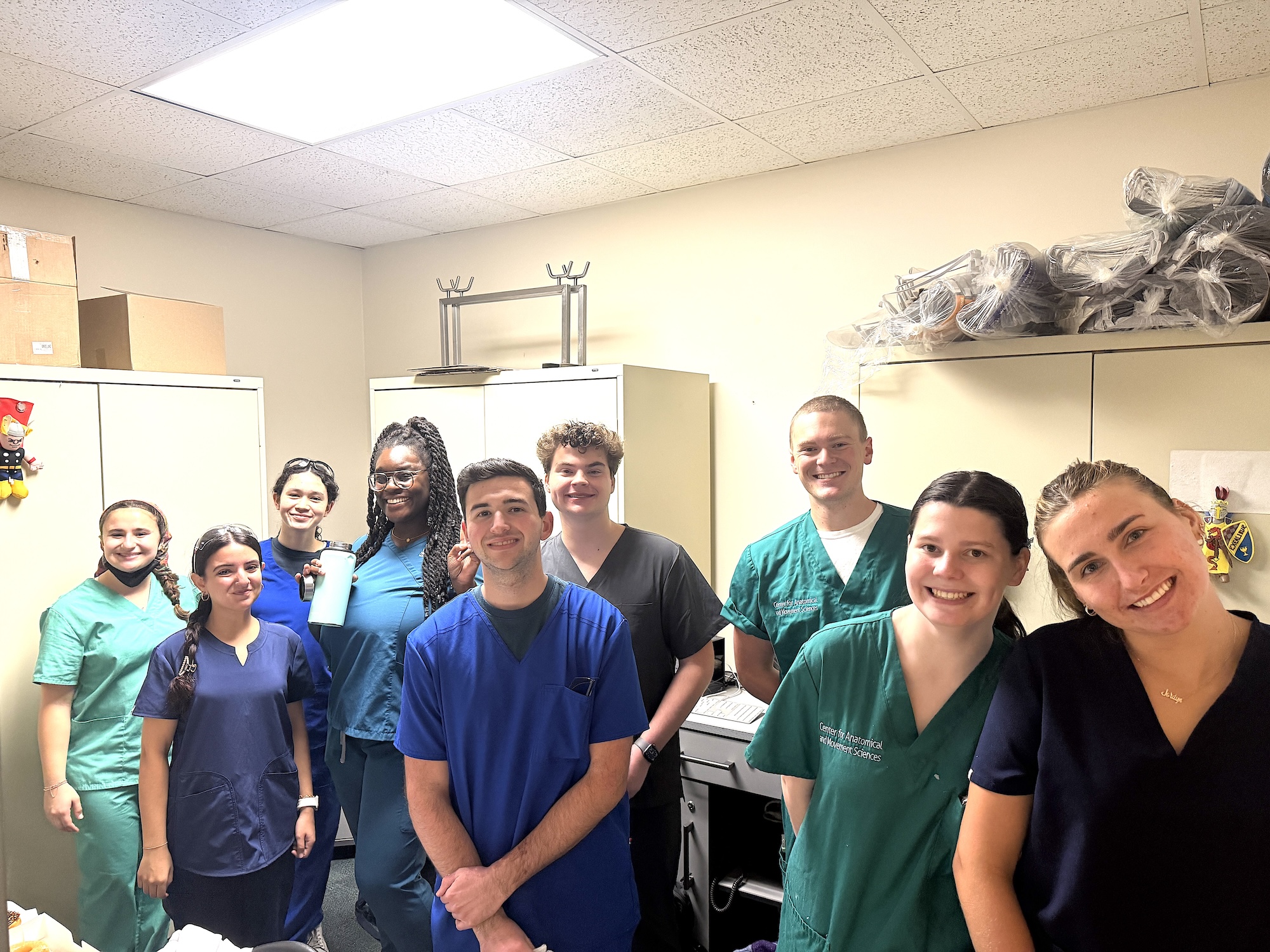 Group of nine medical professionals in scrubs smiling together in an office.