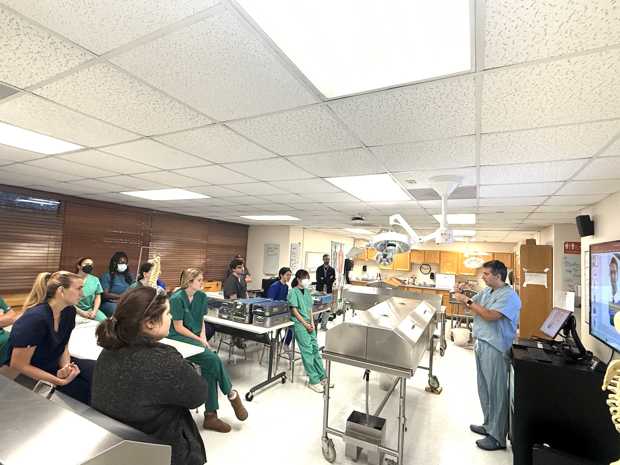 Photograph of students in scrubs listening to an instructor in a medical lab.