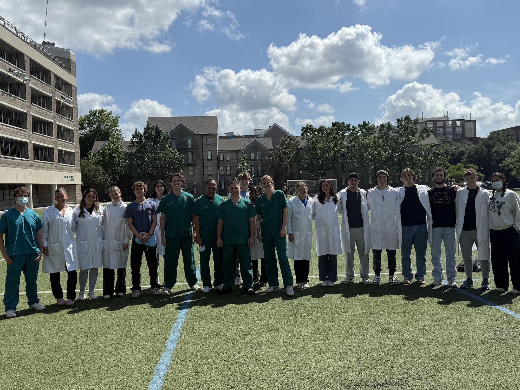 Photograph of a group of medical staff posing on a field on a sunny day.