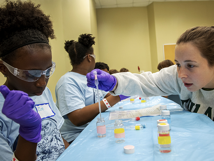 Tulane student assists young girl with a chemistry experiment during GiST. 