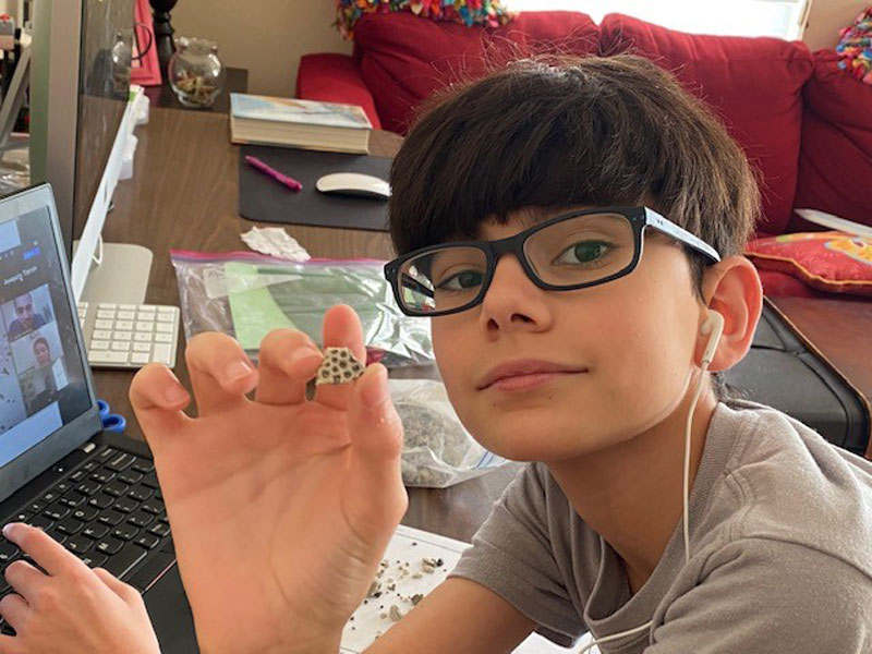 Middle school student participating in virtual BATS program, holding up a fossil.