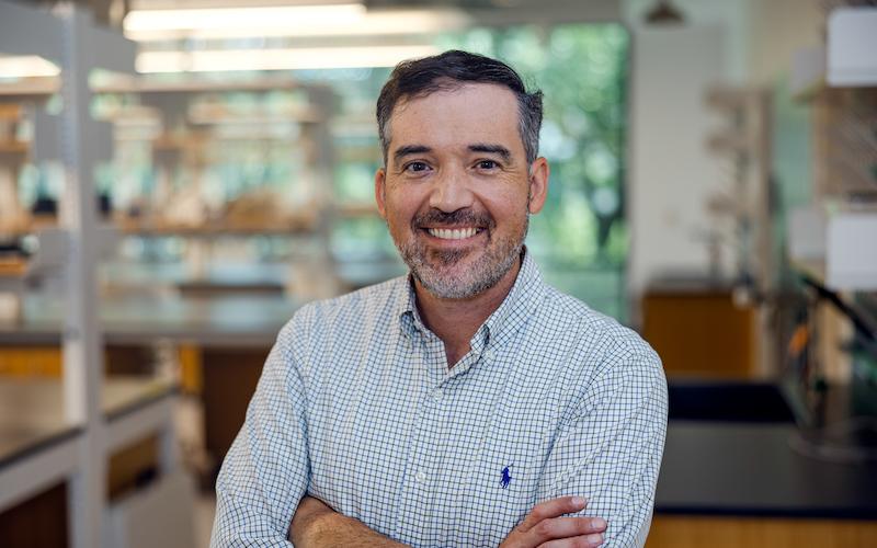 Man with arms crossed, smiling, in a lab coat.
