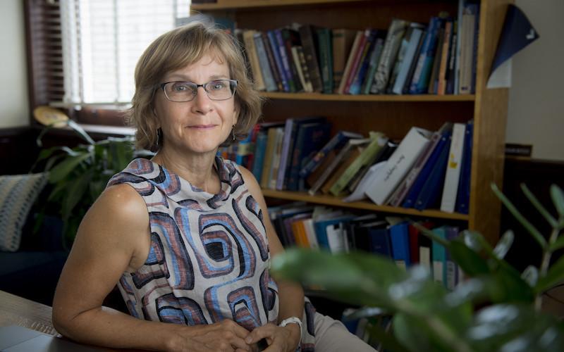 Woman with glasses in front of a bookshelf.