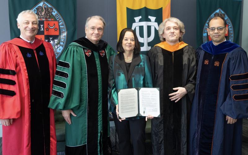 Five academics in regalia stand together, holding a document.