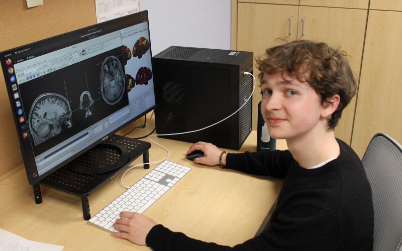 Young person at a desk with a computer displaying brain scans.