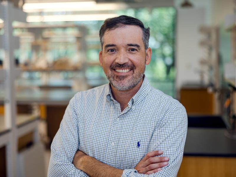 Man with arms crossed, smiling, in a lab coat.