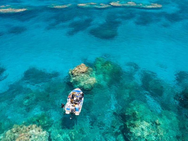 Small boat drifting over a vibrant coral reef.