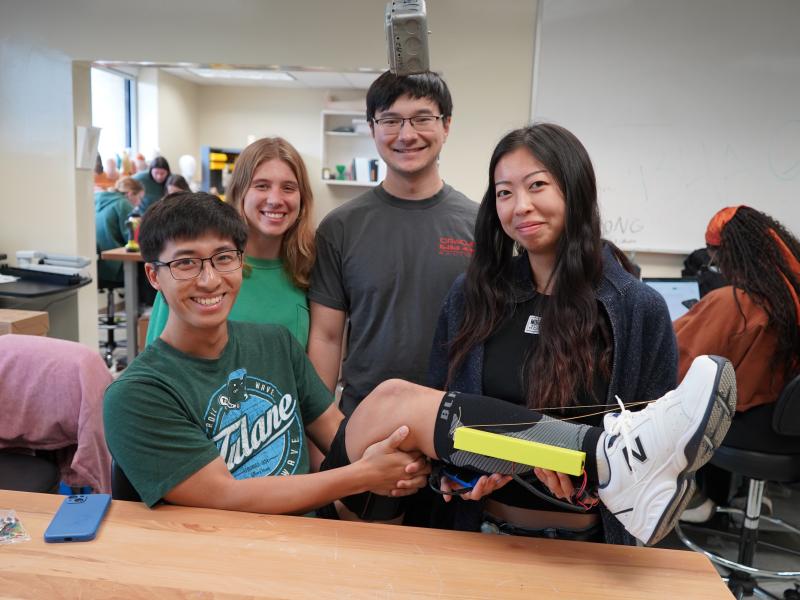 Four smiling young adults in a lab, one holding a prosthetic leg.