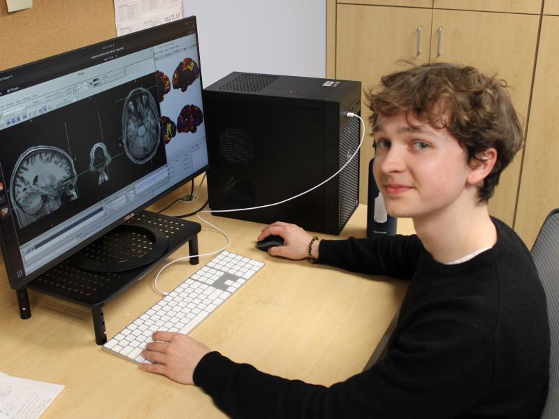 Young person at a desk with a computer displaying brain scans.