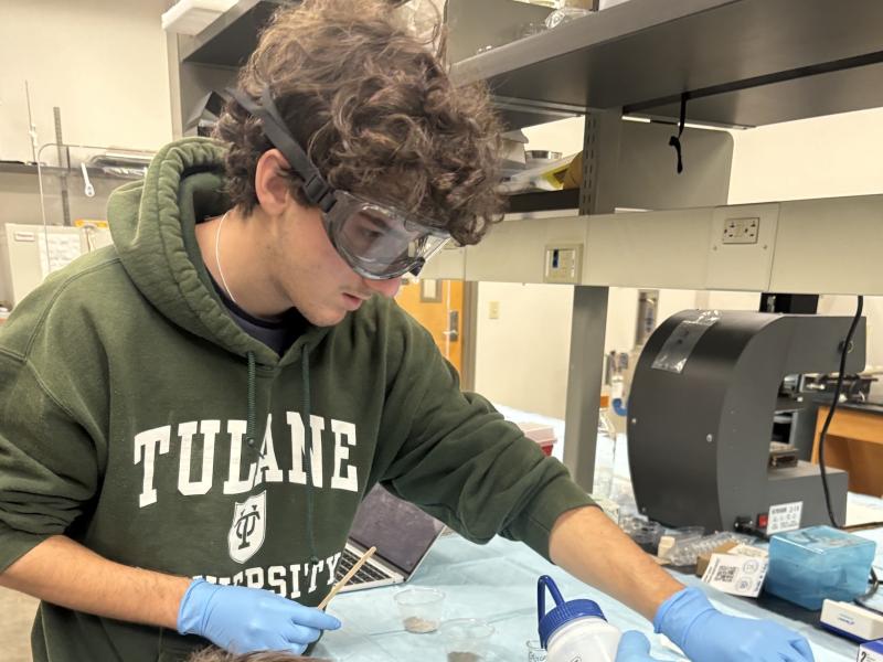 Student in goggles and gloves works at a lab bench.