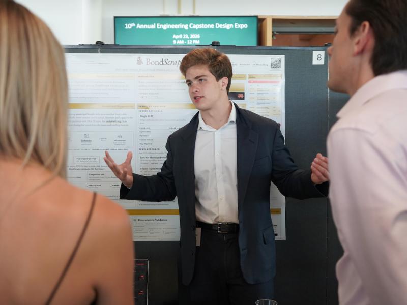 Young man in suit explains poster to two people.