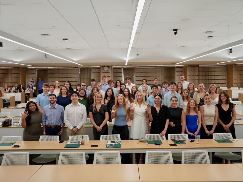 A large group of diverse young adults posing for a photo in a modern classroom.
