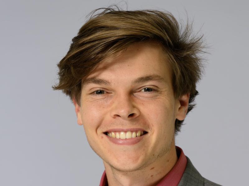Headshot of a smiling young man with messy brown hair.
