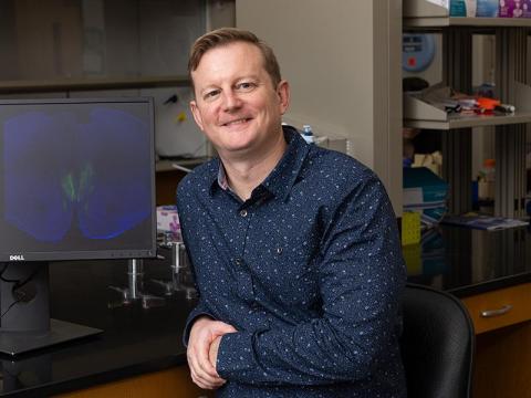 Jonathan Fadok sits by computer screen with an image of a brain.