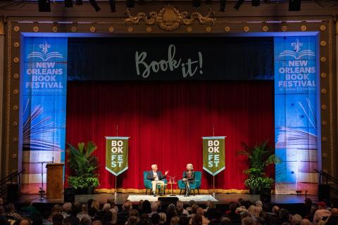 Two men on stage at New Orleans Book Festival with "Book it!" banner.