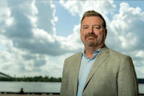 Man in a suit stands with a cloudy sky behind him.