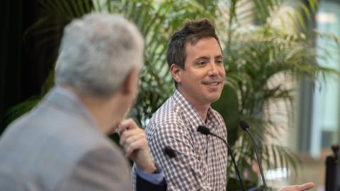 Man in checkered shirt smiles while speaking at a panel.