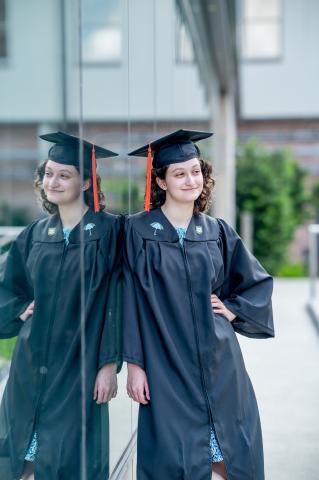Smiling graduate in black cap and gown, reflected in glass.