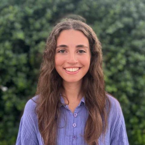 Smiling young woman with long brown hair and a purple shirt.