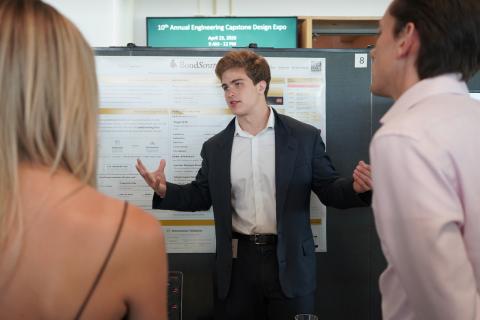 Young man in suit explains poster to two people.