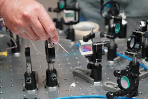 Close-up of a hand adjusting optical equipment on a lab bench.