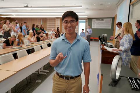 Young man in a blue polo shirt and khakis making a "shaka" hand sign.