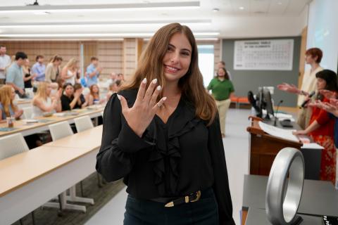 Woman proudly shows off her engagement ring in a classroom.