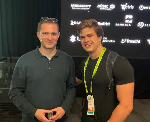 Two men smiling at the camera, with a backdrop of logos.