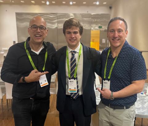 Three men, two older and one young, smile for a photo, all wearing lanyards.