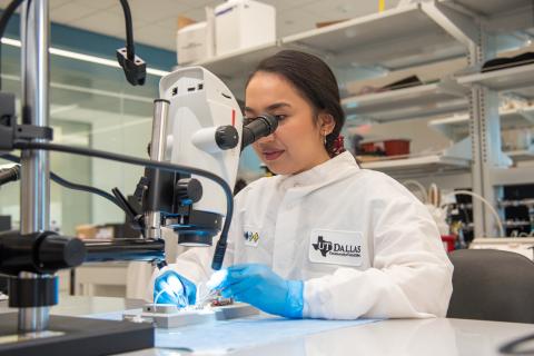 A woman in a lab coat looks into a microscope.