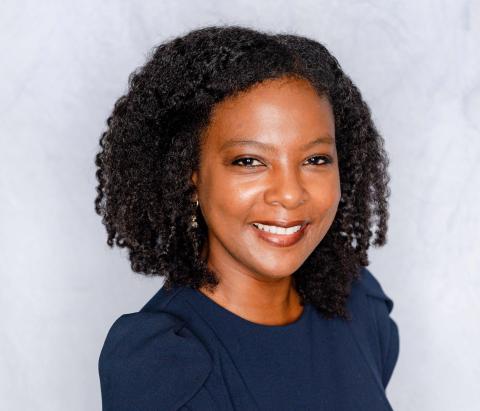 A portrait of a Black woman with dark, curly hair and a bright smile.