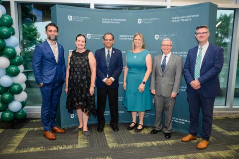 Six people stand in front of a green backdrop at a formal event.