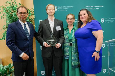 Four people, two men and two women, stand in front of a green backdrop with university logos.