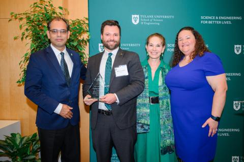 Four people in formal attire pose for a photograph in front of a green backdrop.